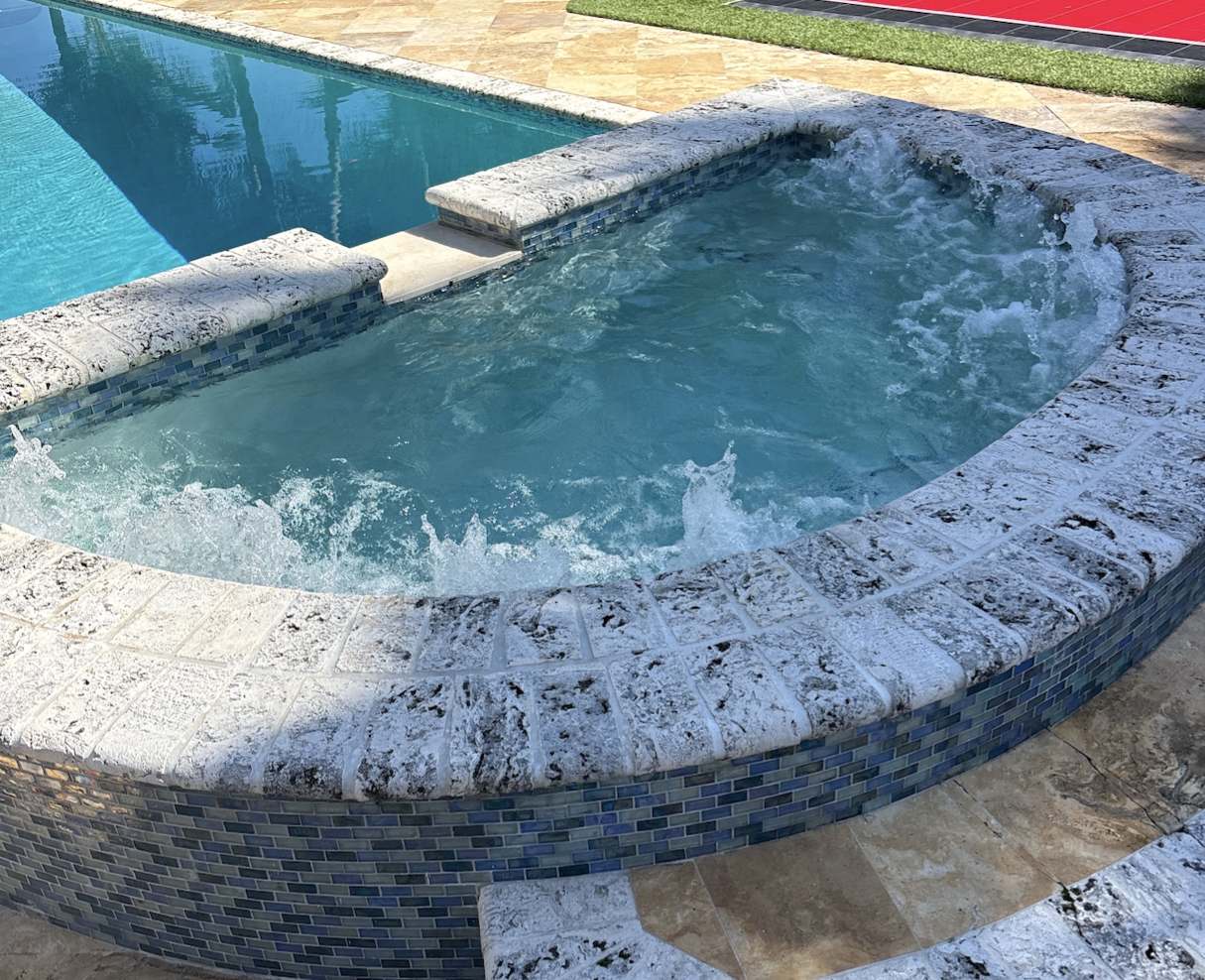 Raised stone spa beside a tiled pool, serviced by Downtown Pools in Fort Lauderdale